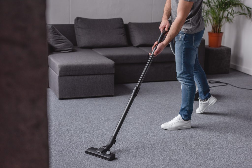 cropped image of man cleaning carpet with vacuum cleaner in living room